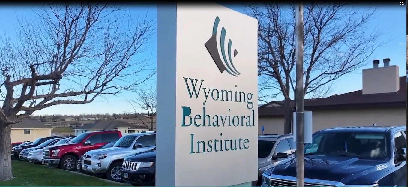 Wyoming Behavioral Institute monument sign outside the Casper facility with parked vehicles and trees in the background