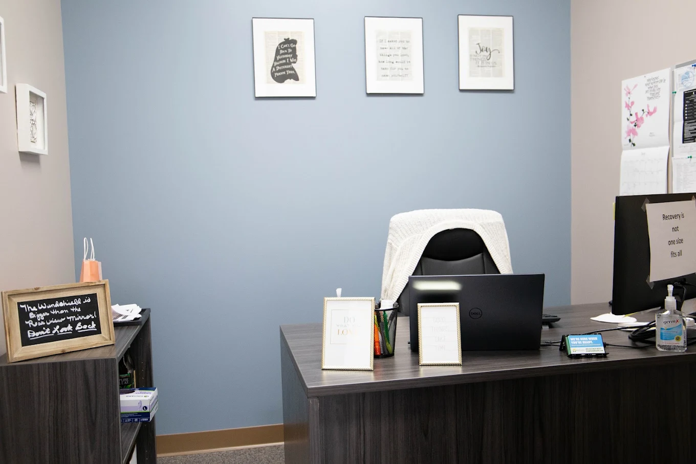 Private consultation office with desk, computer monitors, office chair, framed artwork, and recovery-themed decor