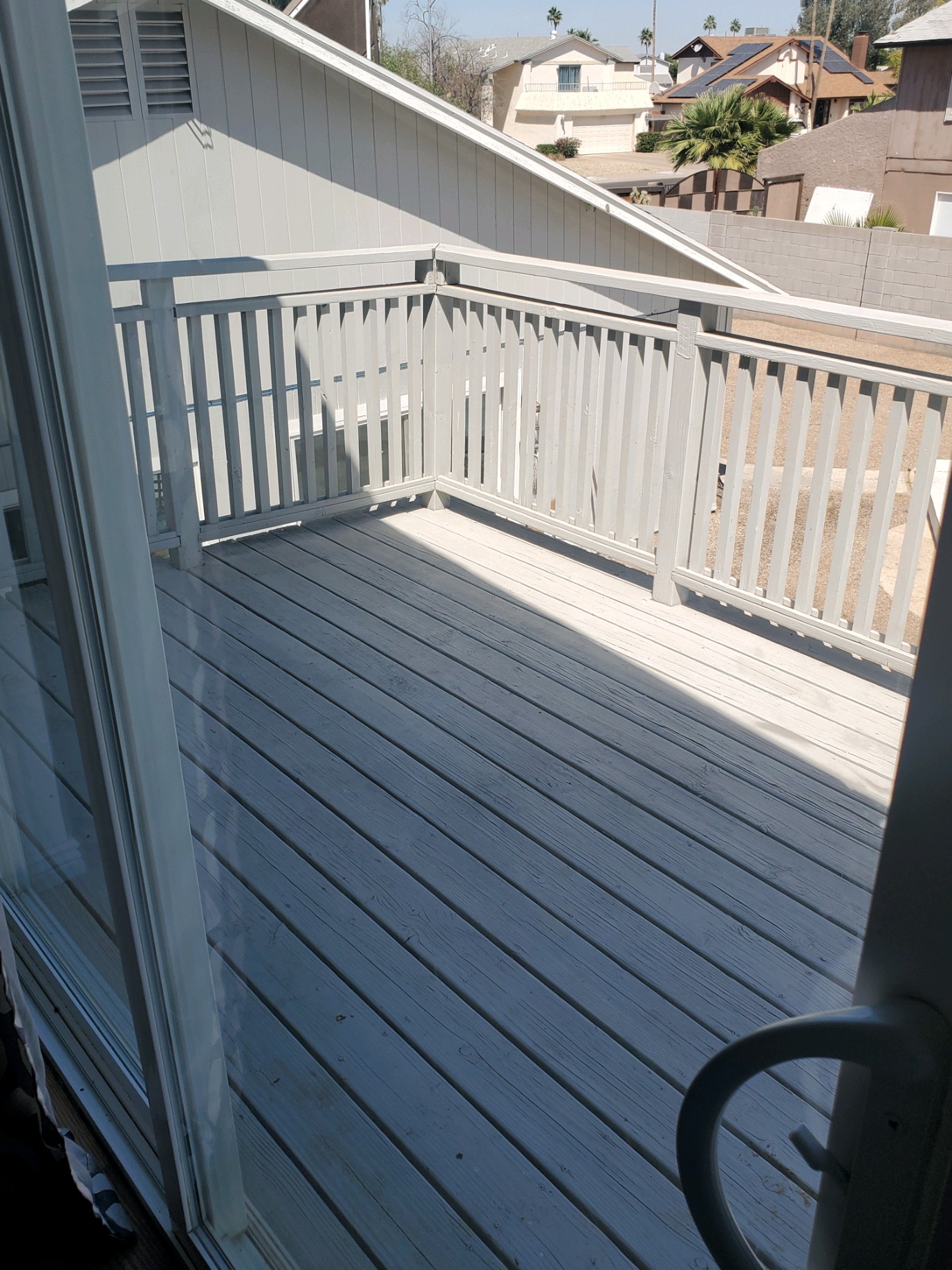 Wooden balcony with railing overlooking rooftops and surrounding homes, accessible from a sliding glass door