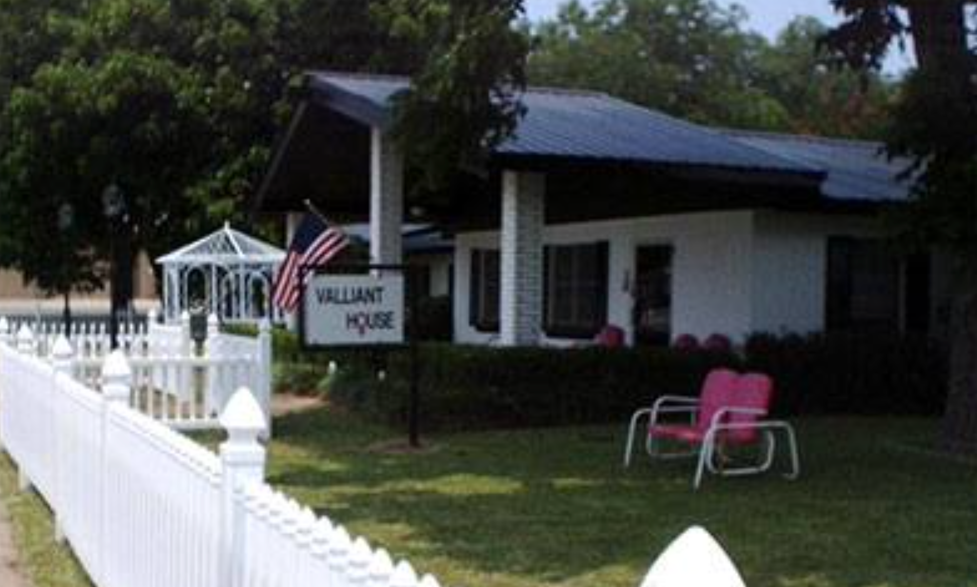 The Valliant House in Konawa features a charming white picket fence, a covered porch with seating, and a small gazebo, creating a welcoming and home-like atmosphere.