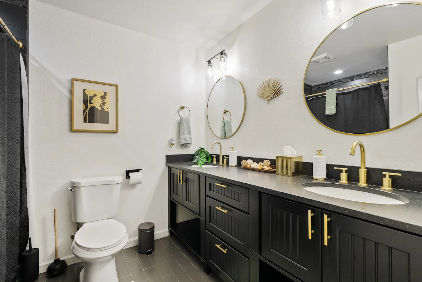 Bathroom with black double vanity, round mirrors, and toilet