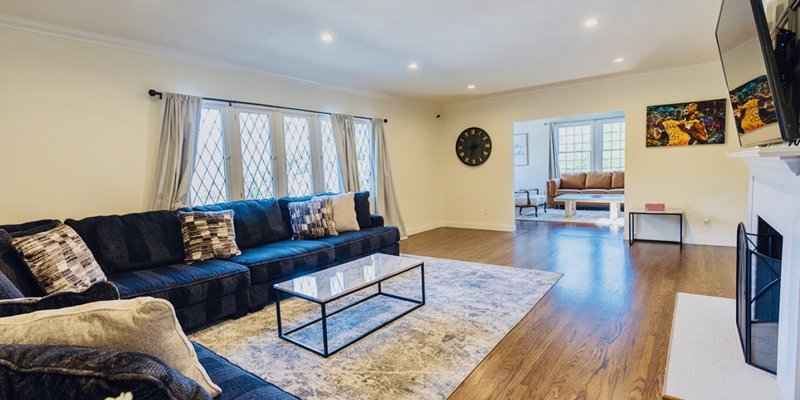 Spacious living room with warm wood floors, a large sectional sofa, and abundant natural light from charming diamond-pane windows.