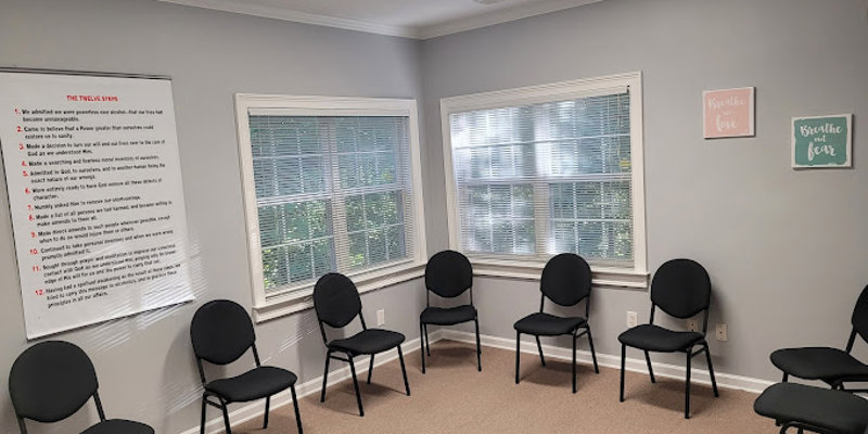 A welcoming group therapy room with a circle of chairs, soft natural light from two windows, and inspirational wall art for a supportive atmosphere.