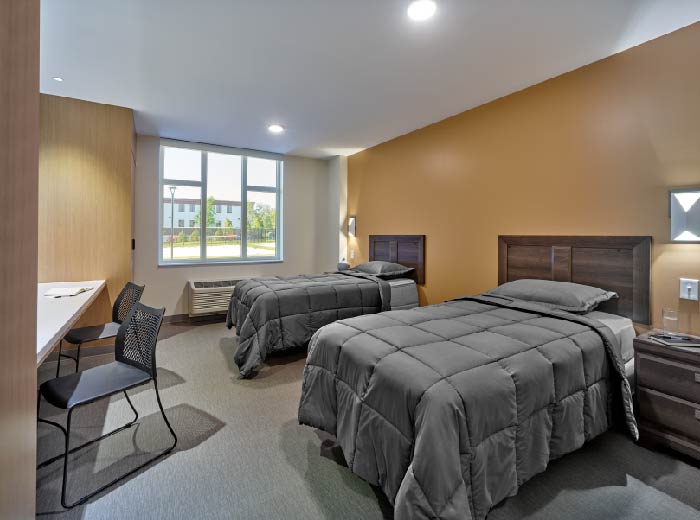 Shared bedroom with two twin beds, sidetables and a long desk.