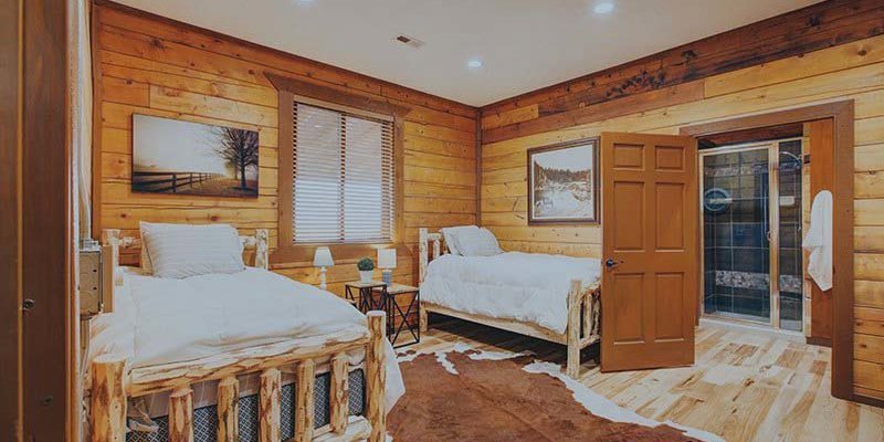 A cozy rustic bedroom with wooden walls, two comfortable log-frame beds, soft lighting, and a warm, inviting atmosphere, perfect for relaxation.