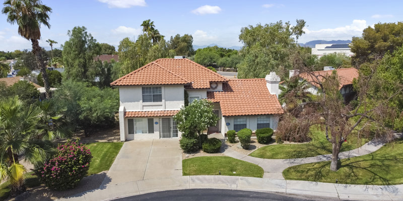 Charming two-story home with terracotta roof, surrounded by lush greenery and a well-manicured lawn, nestled in a peaceful neighborhood.