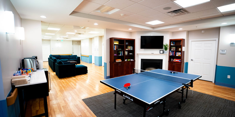 Bright recreational space with a ping pong table, cozy seating area, bookshelves, fireplace, and a snack station, perfect for relaxation.