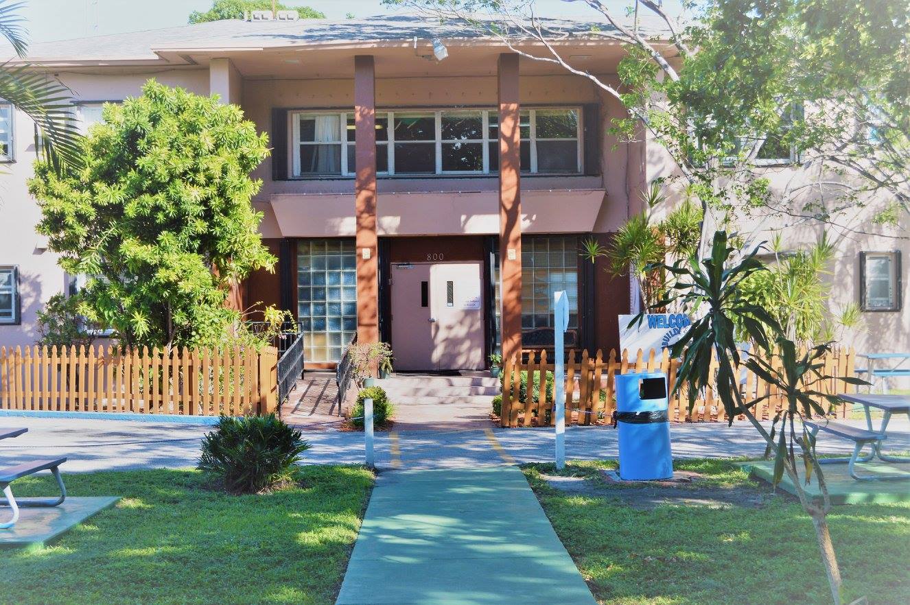 Front view of Better Way of Miami Inc with green walkway, palm trees, and wooden picket fence at the entrance