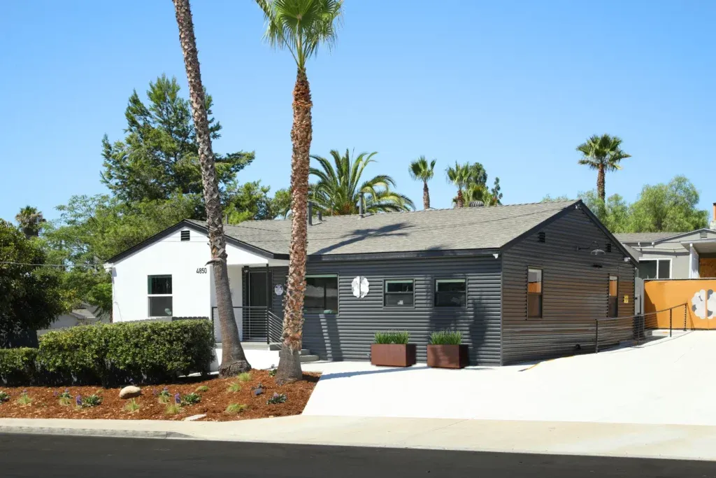Single-story facility with modern dark siding, palm trees, landscaped grounds, and a bright entryway