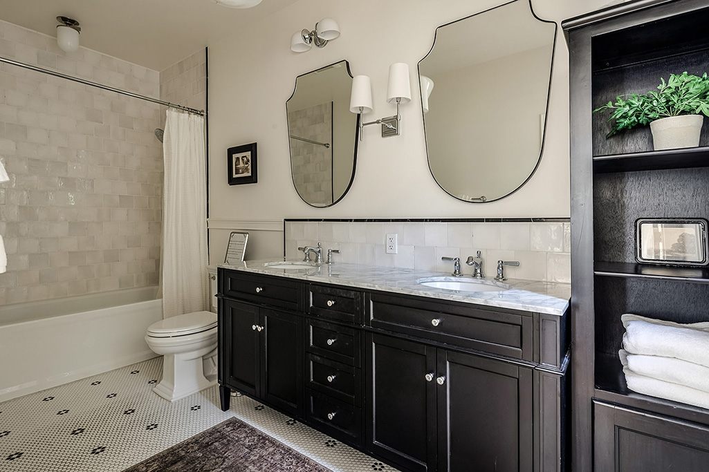 Bright bathroom with black double vanity, marble countertop, and decorative mirrors