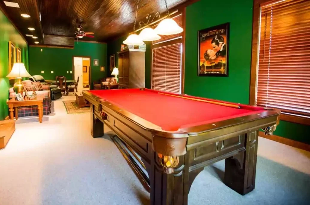 Recreation room with red-felt pool table, green walls, wood ceiling, lounge seating, framed artwork, and pendant lighting