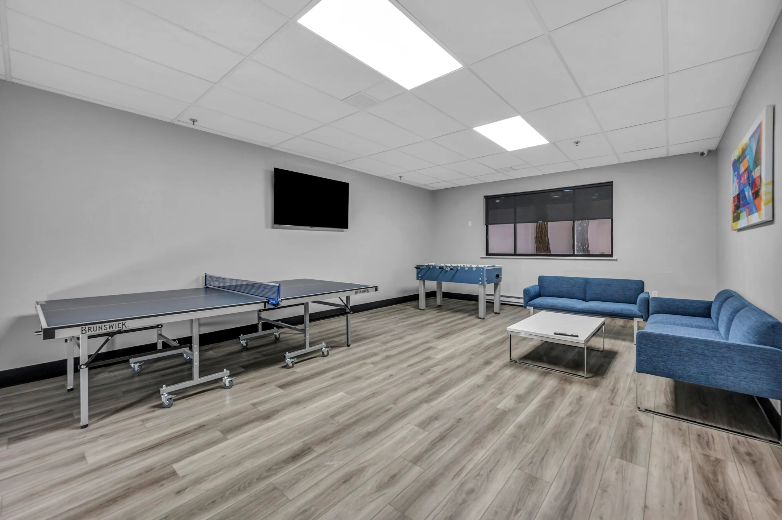 Recreation room with ping pong table, foosball, blue sofas, and wall-mounted TV at Boca Recovery Center Massachusetts