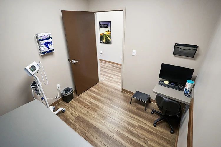 Exam room at BrightView Health Marion with examination table, computer workstation, vital-sign monitoring equipment, medical supplies, and wood-look flooring