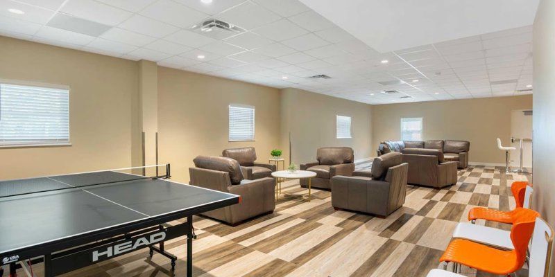 A spacious recreation room with a ping pong table, comfortable leather seating, and vibrant orange chairs, offering a relaxed environment for leisure.