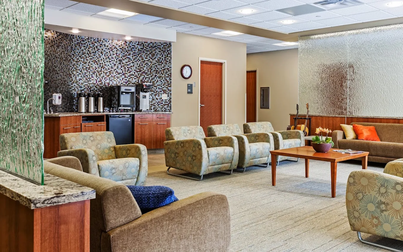 Spacious common area with upholstered seating, coffee station, tables, and textured glass partitions