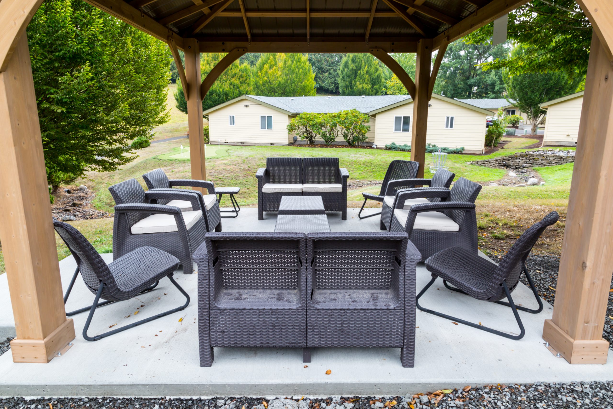 A gazebo with outdoor seating, surrounded by greenery and cottages.