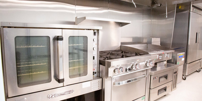 A modern, fully-equipped commercial kitchen with stainless steel appliances, including a large oven, stove, and refrigeration units, ready for meal preparation.