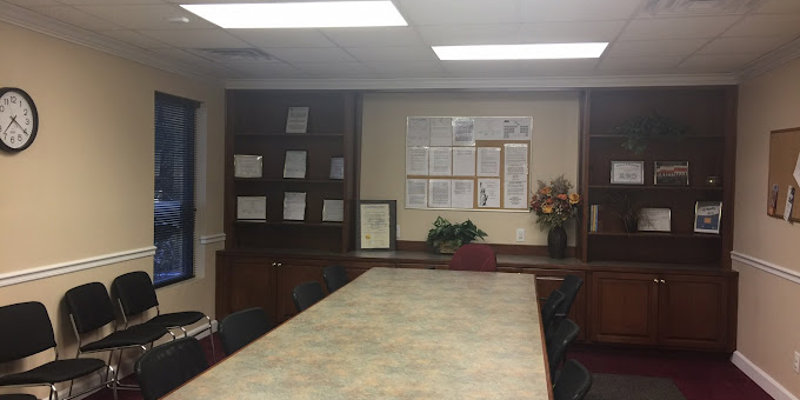 A professional meeting room featuring a large central table, comfortable chairs, and organized shelves, creating a functional and welcoming space.