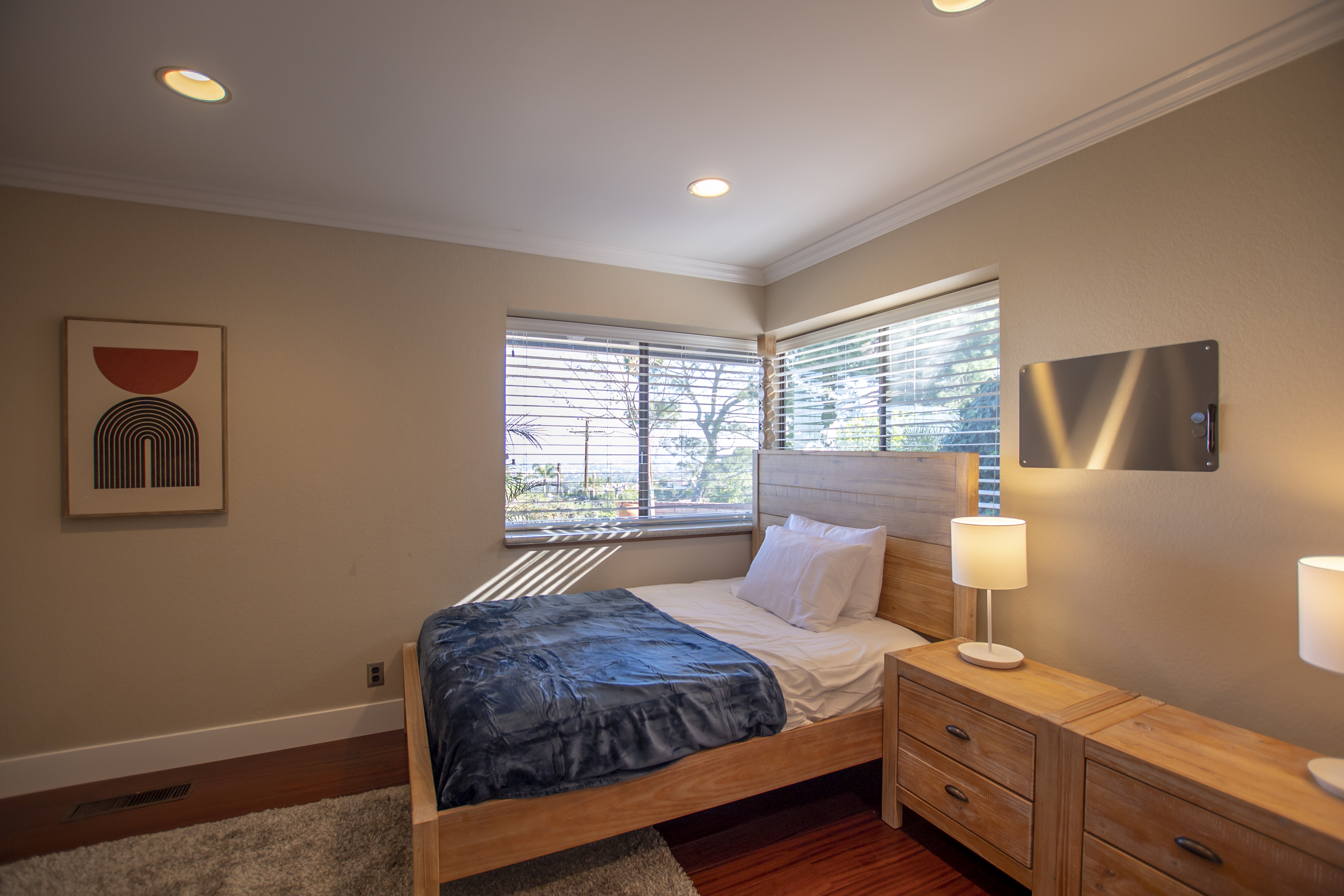 Minimalist bedroom with a wooden bed, soft lighting, and large windows