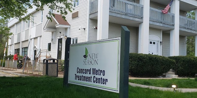 A welcoming colonial-style building with an American flag, surrounded by lush greenery, housing the New Season Concord Metro Treatment Center.