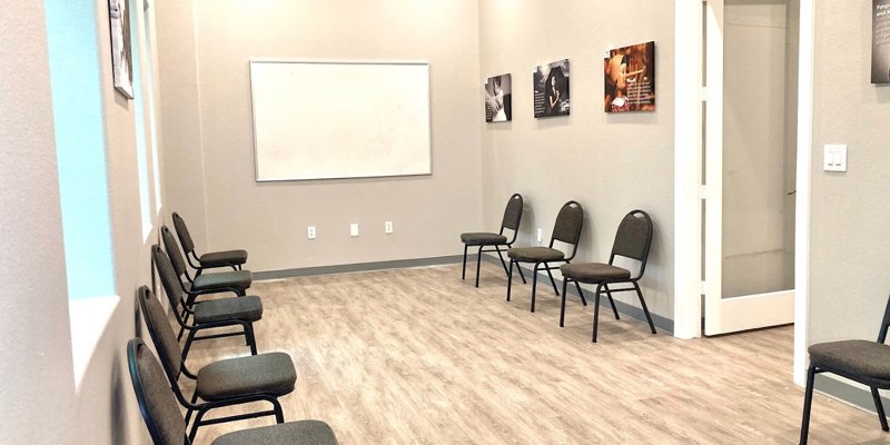 A bright, spacious meeting room with comfortable chairs arranged for group sessions. The room features a whiteboard and inspiring wall art.