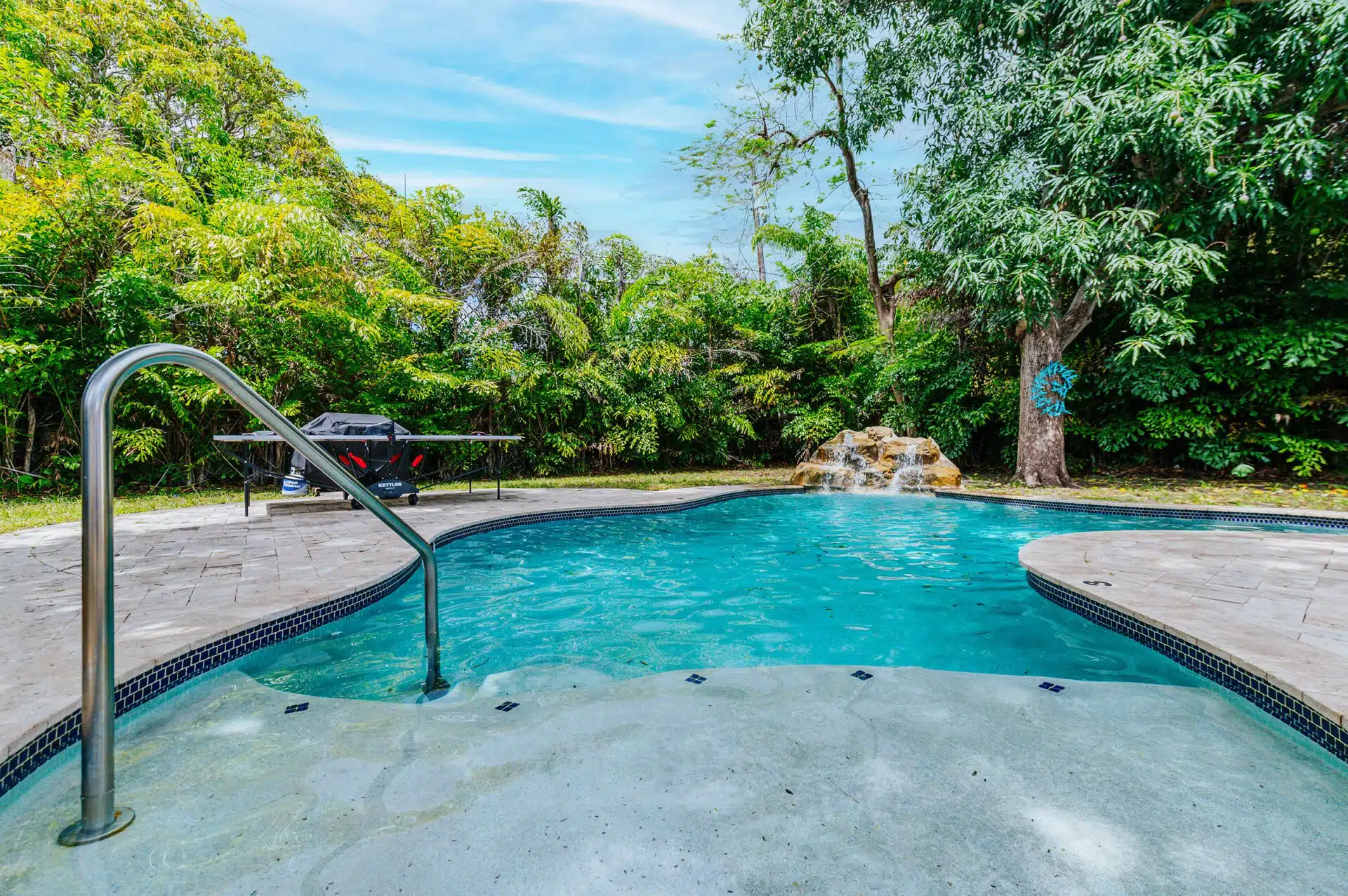Backyard pool with waterfall feature and trees in the background