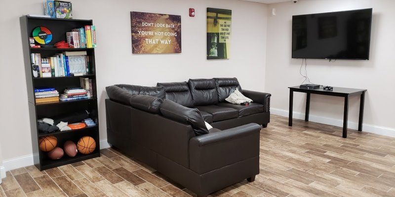  A cozy recreation room featuring a comfortable leather sectional, a large TV, a bookshelf with games and books, and motivational wall art.