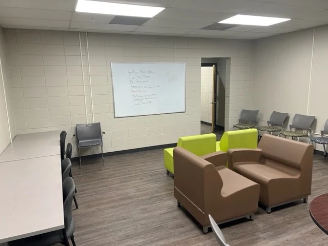 Group meeting room with sofas, chairs, tables, and a whiteboard at Red River Treatment Center