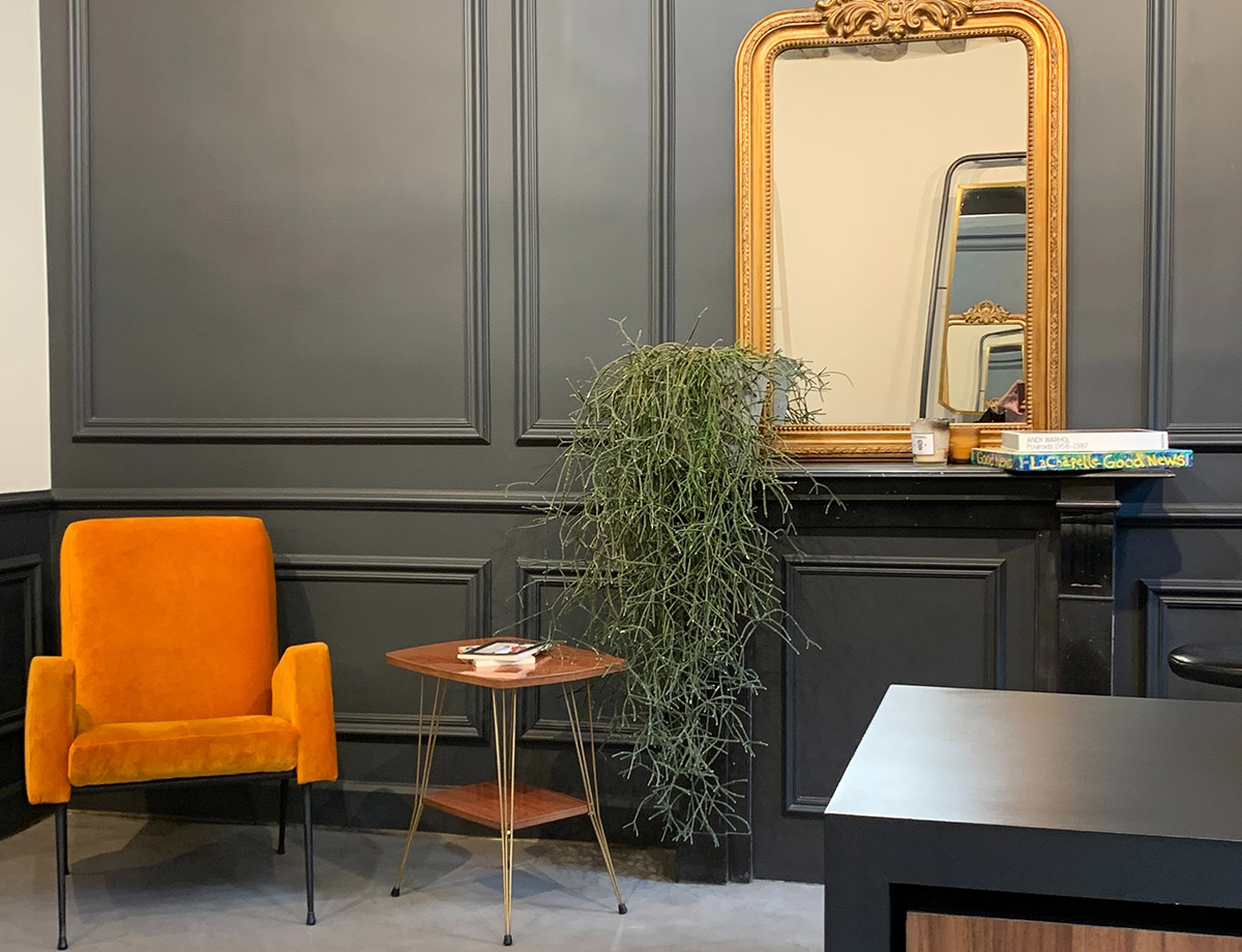 Cozy reception with orange chair and gold mirror on dark paneled wall.