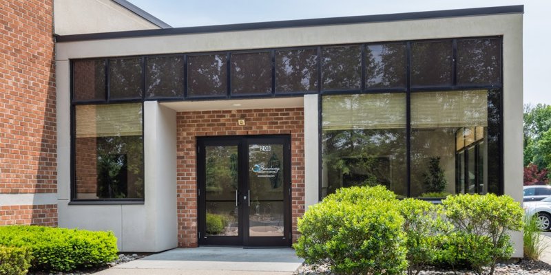 The image shows the entrance of a modern outpatient center with large windows and a brick facade, surrounded by neatly maintained shrubs and greenery.