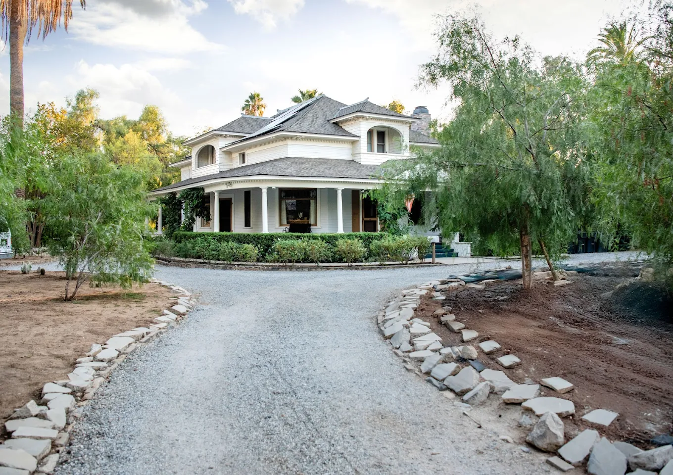 Tree-lined gravel driveway leading to a large white recovery home with wrap-around porch