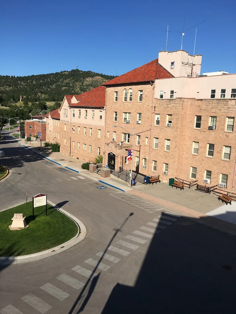 Multi-story stone VA campus building with red roof and benches