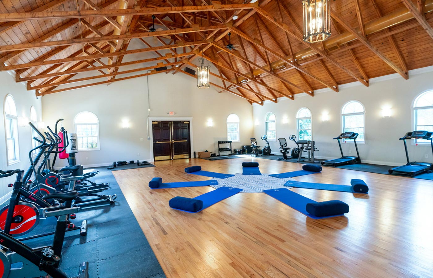 Bright gym with exercise machines and mats in a spacious wood-beam room.