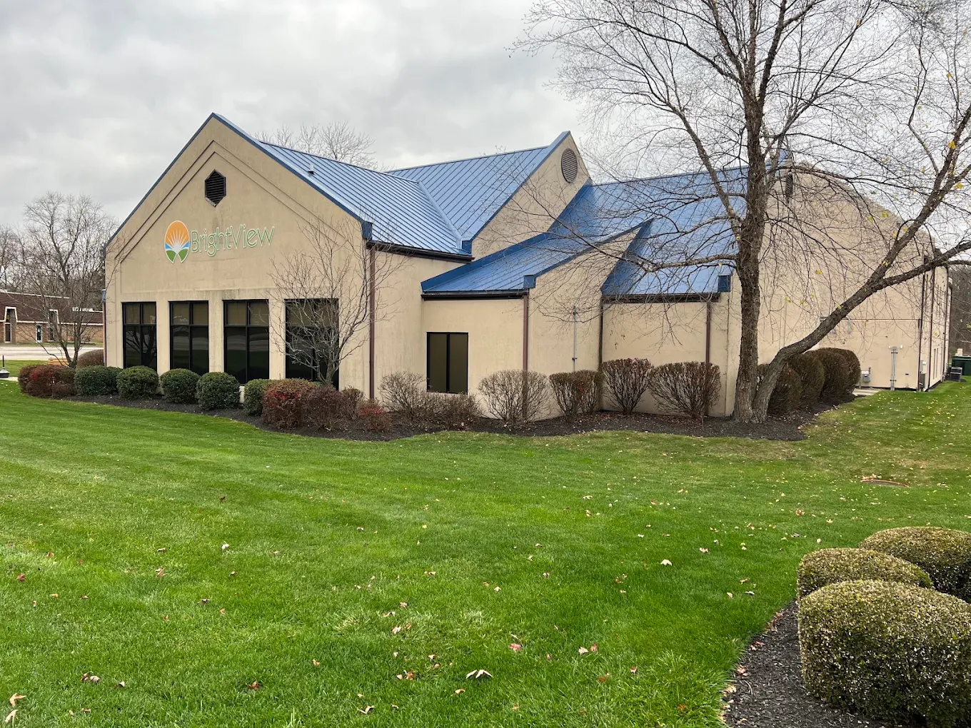 Exterior of BrightView Health in Kent, Ohio, showing the beige building with blue metal roof, BrightView signage, landscaped lawn, shrubs, and trees