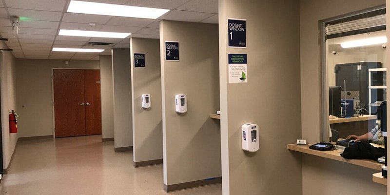  A clean hallway featuring numbered dosing windows, hand sanitizer stations, and soft lighting, providing a calm and orderly environment for service.