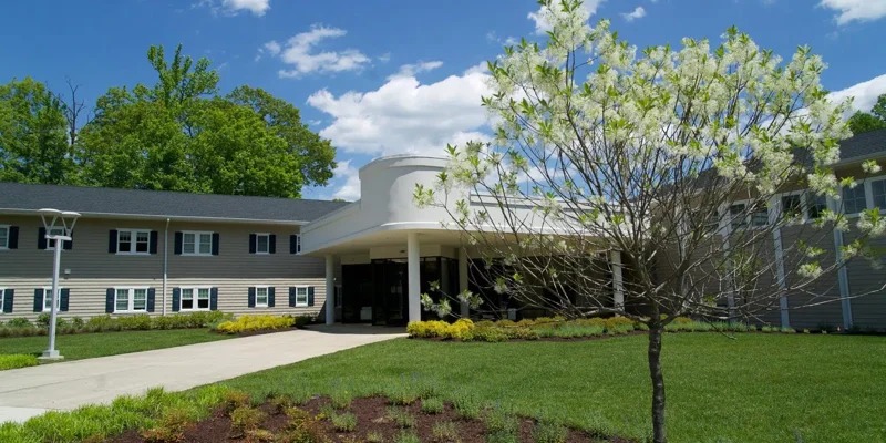 Welcoming rehabilitation center with a modern entrance, well-maintained landscaping, blooming trees, and a bright, sunny day, creating a peaceful atmosphere.