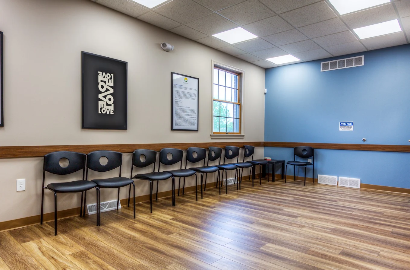 BrightView Health Youngstown lobby with a row of black waiting chairs, framed wall displays, large window, blue accent wall, and wood-look flooring