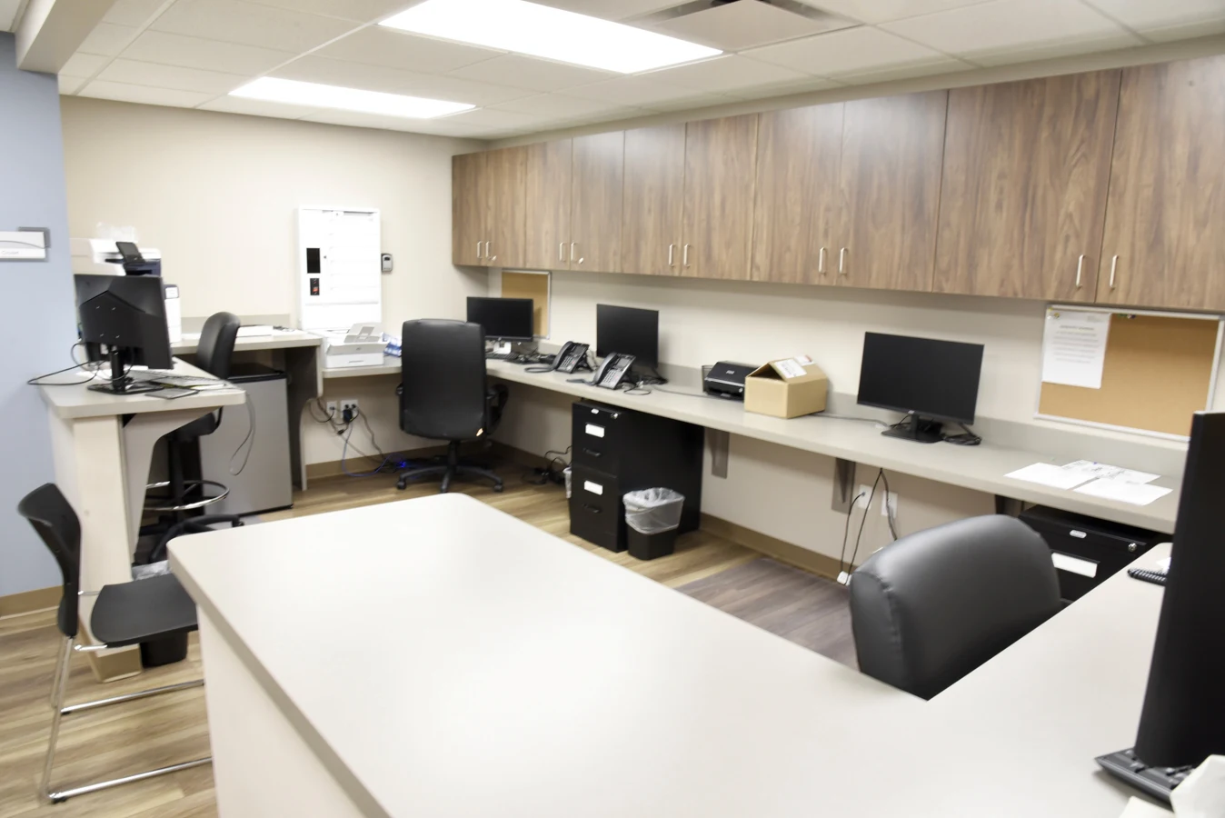 BrightView Health staff workstation with multiple computers and telephones, long counter, overhead wood cabinets, office chairs, and central work surface