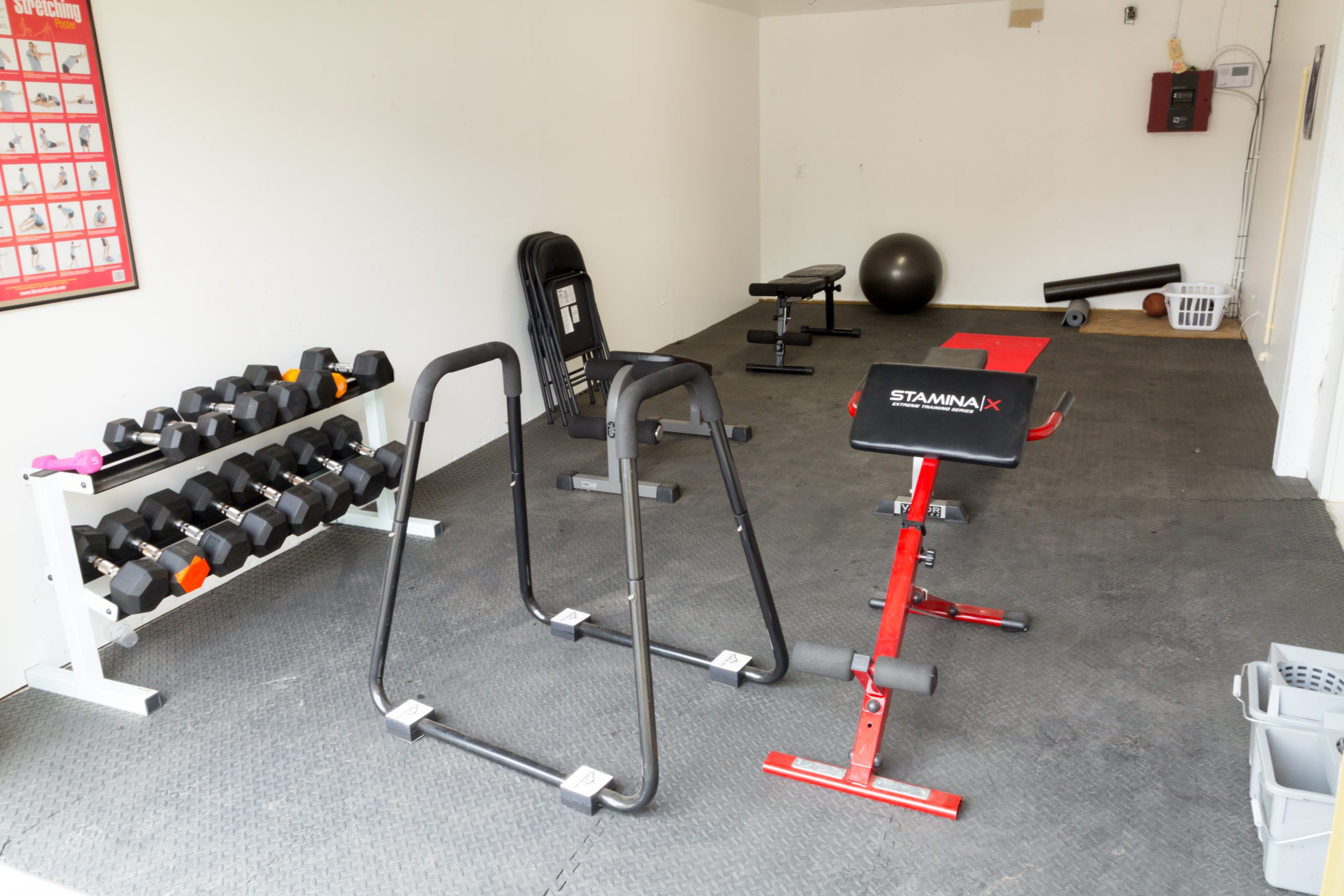A small gym with weights, exercise equipment, and mats.