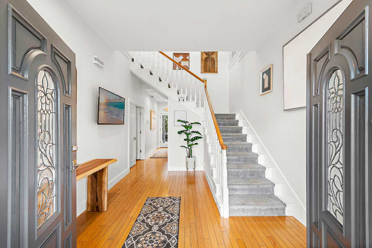 Welcoming entry lobby with decorative double doors, hardwood flooring, staircase, runner rug, wall art, and indoor plant