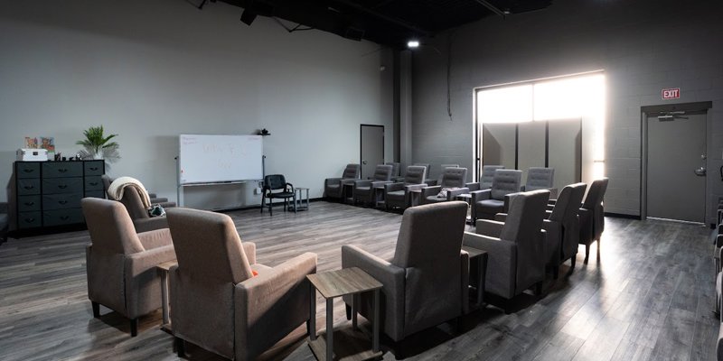 Spacious group therapy room with comfortable chairs arranged in a circle, soft lighting, and a whiteboard, creating a supportive environment.