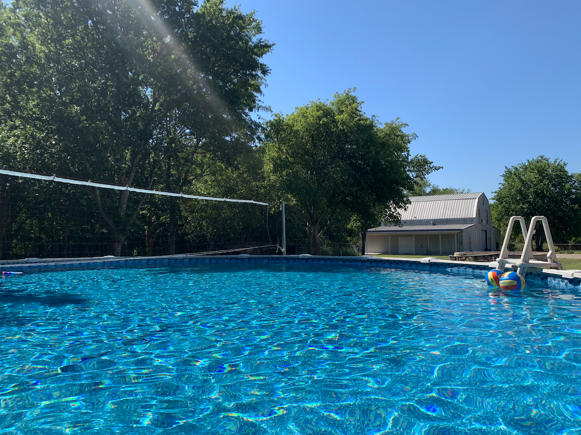 Outdoor swimming pool at Discovery Point Retreat Waxahachie surrounded by trees with a volleyball net and pool ladder