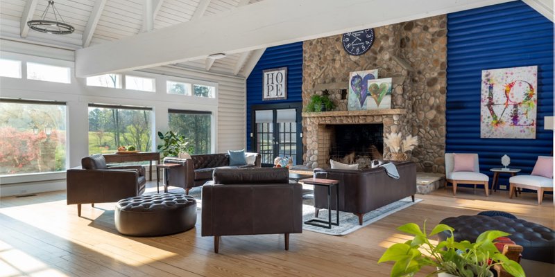 A bright, airy lounge with vaulted ceilings, large windows, and a cozy stone fireplace. Comfortable seating and warm decor create a welcoming ambiance.