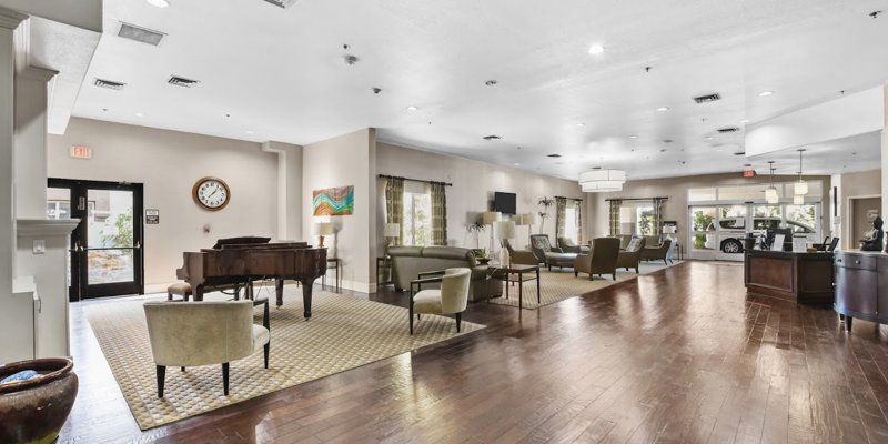  A bright, elegant common area with polished wood floors, cozy seating, natural light, and a grand piano, fostering a peaceful ambiance.