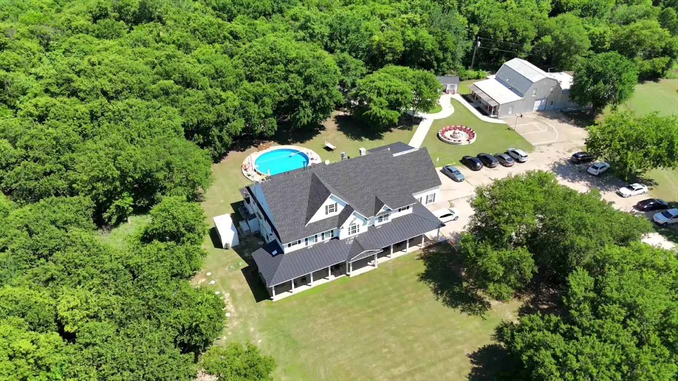Aerial view of Discovery Point Retreat Waxahachie showing the main residence, swimming pool, recreational building, lawns, and surrounding woodland