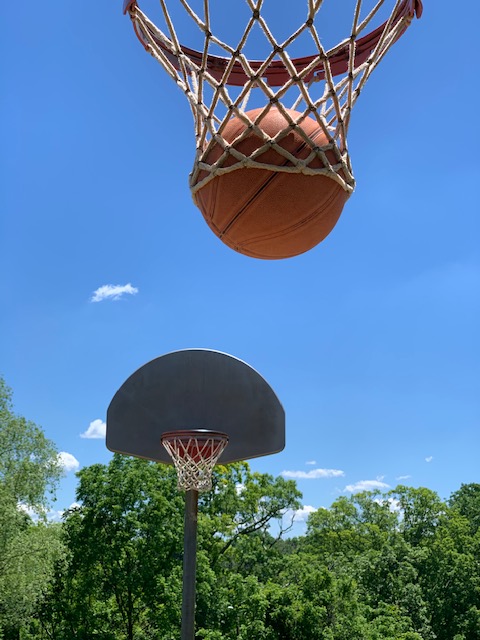 Basketball going through hoop on outdoor court under blue sky