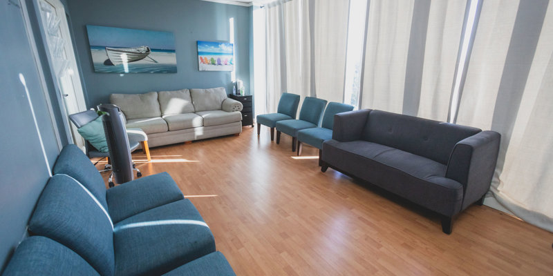 A bright, comfortable room with a mix of blue and gray seating, featuring a cozy sofa and chairs. Beach-themed artwork adds a relaxing touch to the space.