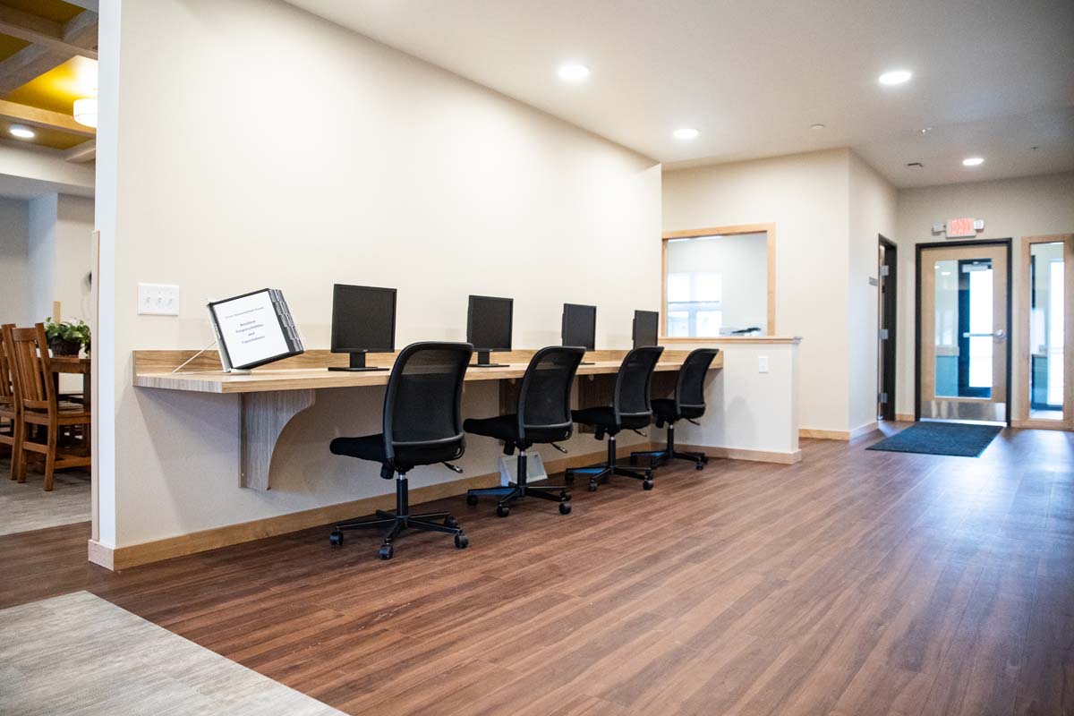 Row of computer stations with chairs along a hallway wall