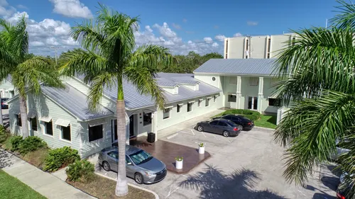 Palm tree-lined rehab facility with light green buildings and parking