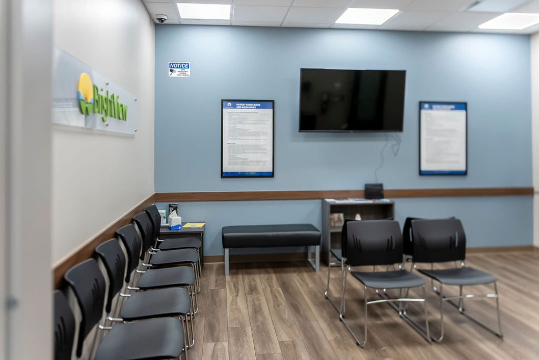 BrightView Health waiting area with rows of black chairs, bench seating, wall-mounted television, and blue accent wall